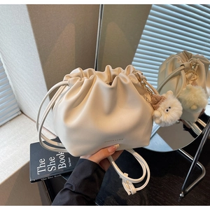 Detail of creamy white pleated bucket bag with plush lamb pendant and drawstring closure