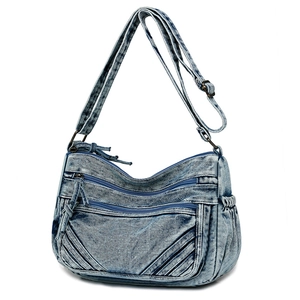 Detail view of washed blue denim crossbody bag with multiple zippers and bronze hardware