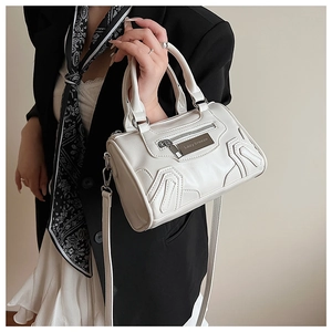 Primer plano del bolso beige cilíndrico con cremallera plateada y placa de metal pulido