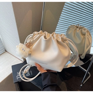 Detail of cream pleated bucket bag with drawstring closure and cute plush charm
