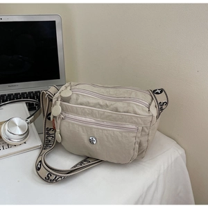 Macro detail of beige nylon crossbody bag with multiple zippers and patterned strap