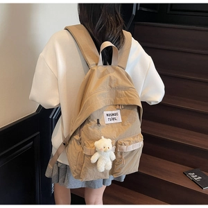 Khaki canvas backpack detail featuring a cute plush bear pendant and front pocket design