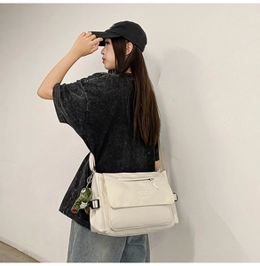 Detail of off-white crossbody messenger bag with flap closure and green frog pendant