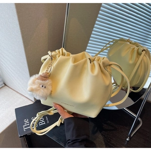 Detail of pale yellow drawstring bucket bag with pleats and cute plush doll pendant