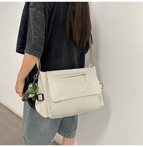 Detail of off-white nylon messenger bag featuring an adjustable strap and green dinosaur charm