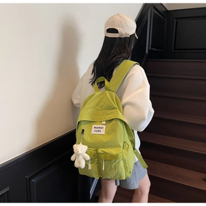 Zaino leggero in tela verde chiaro con ciondolo a forma di orso indossato da una modella