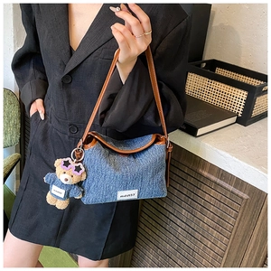 Detail of blue denim bucket bag with brown handle and cute bear doll charm accessory