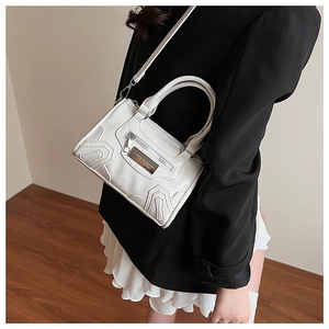 Detalle del bolso almohada de cuero sintético blanco con costuras geométricas y logo plateado
