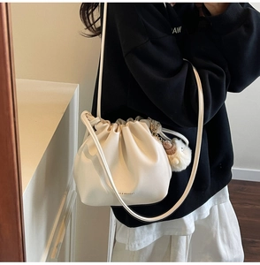 Detail view of cream pleated drawstring bucket bag with plush charm and long strap
