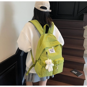 Dettaglio dello zaino in tela verde lime con ciondolo a forma di orso e tasche anteriori