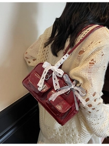 Glossy burgundy leather shoulder bag with lace bow and heart charm detail on model