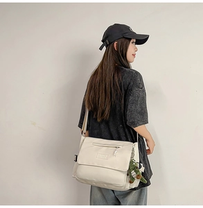 Detail view of large cream messenger bag with nylon texture and cute crocodile pendant