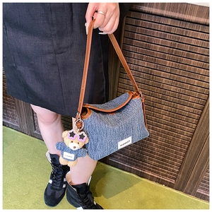 Detail of blue denim bucket bag with brown leather strap and cute plush bear charm