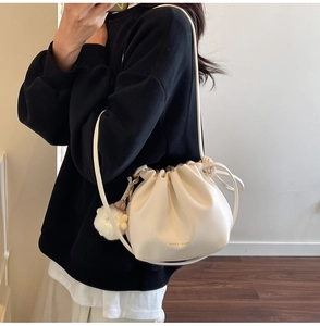 Detail of cream drawstring bucket bag featuring soft leather texture and plush pom-pom charm