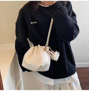 Detail view of cream pleated bucket bag with plush pompom charm on a leather shoulder strap