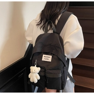 Close-up of black canvas backpack on model featuring a white plush bear charm