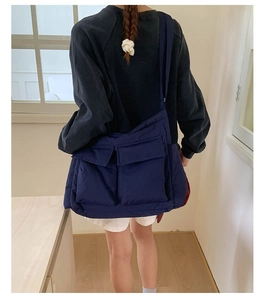 Detail of a large navy blue quilted messenger bag worn as a crossbody on a shoulder