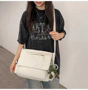 Close-up of minimalist white messenger bag with a green dinosaur plush keychain