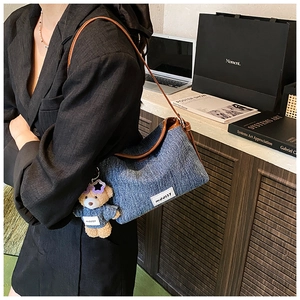 Chic denim bucket bag with brown leather trim and cute teddy bear charm on model's shoulder