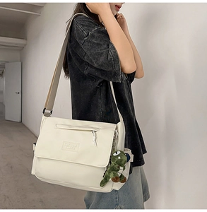 Detailed view of cream messenger bag with wide strap and cute dinosaur keychain accessory