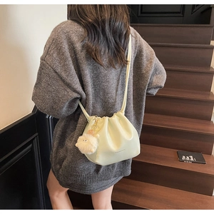 Detail of mint green pleated drawstring bucket bag with a plush white pendant on stairs