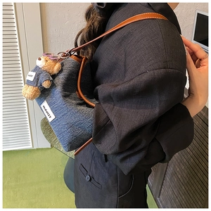 Detail of dark blue denim bucket bag with brown leather strap and cute bear charm