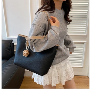 Gros plan sur un sac cabas noir grainé avec anses kaki contrastées et breloque fleur perle