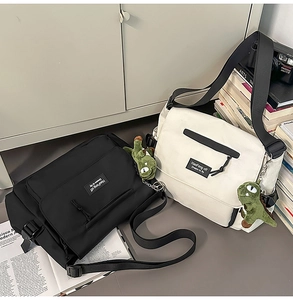 Detailed view of canvas messenger bags in black and beige with dinosaur pendants