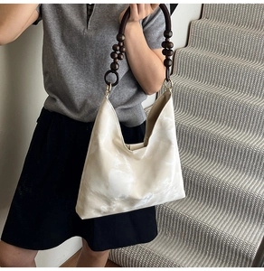 Detail of hobo bag featuring dark brown wooden bead strap and creamy leather finish