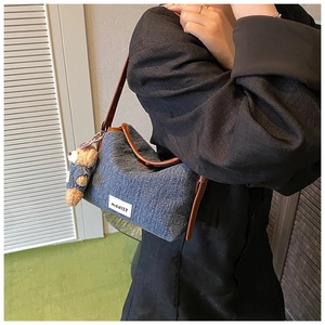 Close-up of denim shoulder bag with brown leather trim and a cute plush bear charm