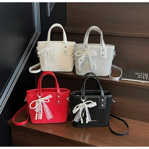 Detail showing various colors of bucket bags with lace pearl bow charms on a dark display