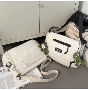 Detail of white canvas messenger bags with a green dinosaur plush charm on a storage cabinet