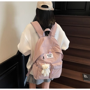 Detail view of pink canvas backpack with plush bear charm and spacious zipper compartments