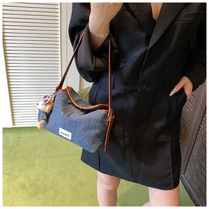 Detail of blue denim shoulder bag with brown leather trim and a cute teddy bear charm