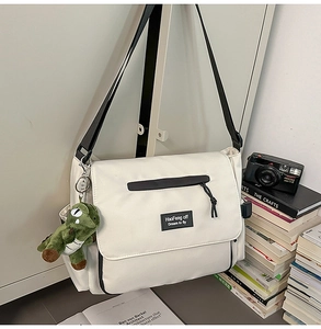 White nylon messenger bag featuring a green plush dinosaur charm and black strap