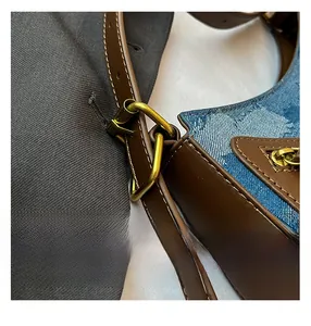 Detail of blue denim and brown leather patchwork bag with golden buckles and stitching
