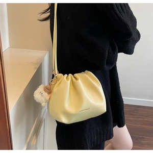 Detail of pale yellow pleated bucket bag with plush sheep charm and fashion text print