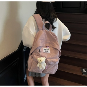 Pink canvas backpack with white bear pendant and letter patch on dark wooden steps