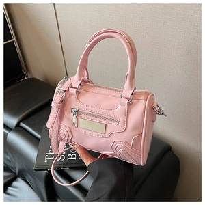 Detalle de bolso bandolera de cuero rosa con cremallera plateada sobre un sofá negro
