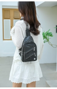 Detail of black faux leather chest bag with geometric strap and decorative zippers