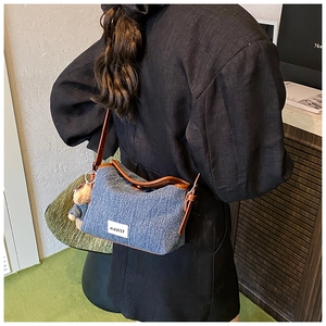 Blue denim bucket bag shown on shoulder with brown leather trim and bear charm