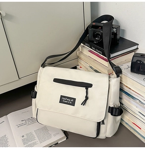 Close-up of canvas messenger bag with logo patch and vintage camera on books