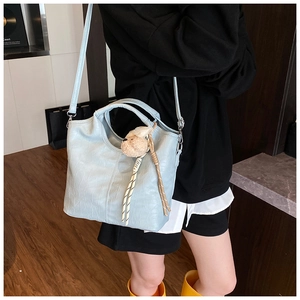 Detail view of light blue crocodile embossed tote bag worn as a crossbody with bear charm