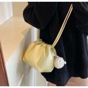 Detail view of yellow pleated bucket bag with cute white plush ball charm on strap