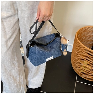 Close-up of blue denim bucket bag with teddy bear charm and black leather strap details