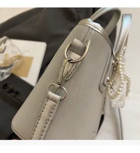 Detail of silver bucket bag with metallic texture, pearl lace bow, and polished hardware