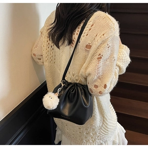 Detail of black pleated drawstring bucket bag with plush charm and shoulder strap