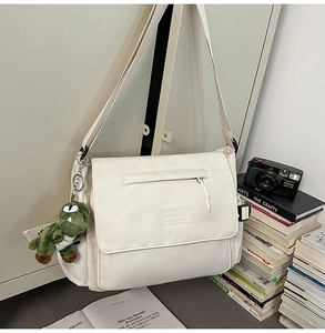 Detail of a beige messenger bag with a plush dinosaur charm in a cozy study setting