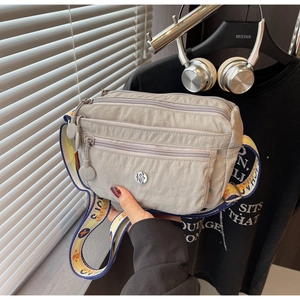 Detail of grey nylon crossbody bag featuring multi-zipper pockets and colorful floral strap