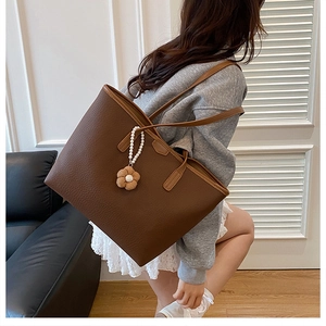 Sac cabas en cuir marron avec pendentif fleur de perle porté par un mannequin chic